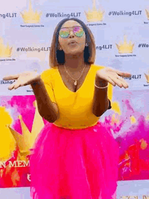 a woman in a yellow shirt and a pink skirt is standing in front of a wall with crowns on it .