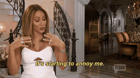 a woman in a white dress is sitting in front of a staircase in a living room and talking .