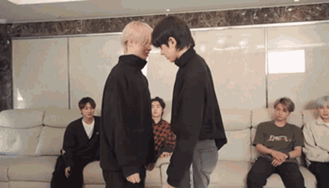 two men are standing next to each other in a living room and holding hands .
