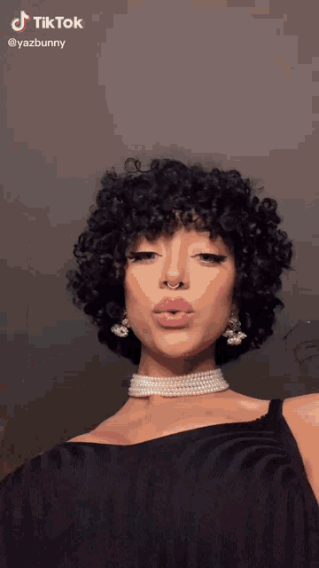 a woman with curly hair is wearing a pearl choker