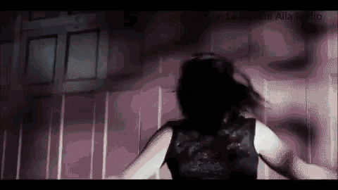 a woman in a black tank top is standing in front of a pink wall in a dark room .
