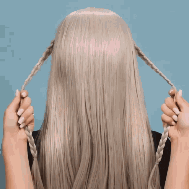 a woman with long blonde hair is braiding it in a ponytail