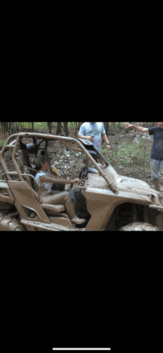 a man is sitting in a muddy atv while two other men stand nearby