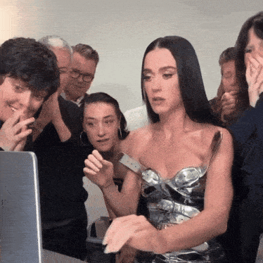 a group of people are standing around a woman in a silver dress