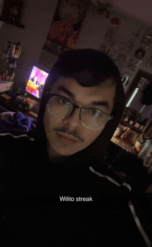 a man wearing glasses and a black hoodie has wilito streak written on his face