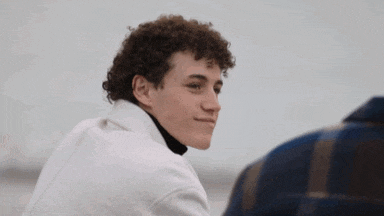 a young man with curly hair is looking at another man in a plaid shirt