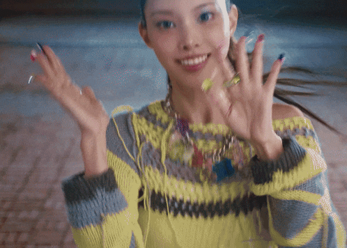 a woman wearing a yellow and gray sweater is smiling with her hands in the air