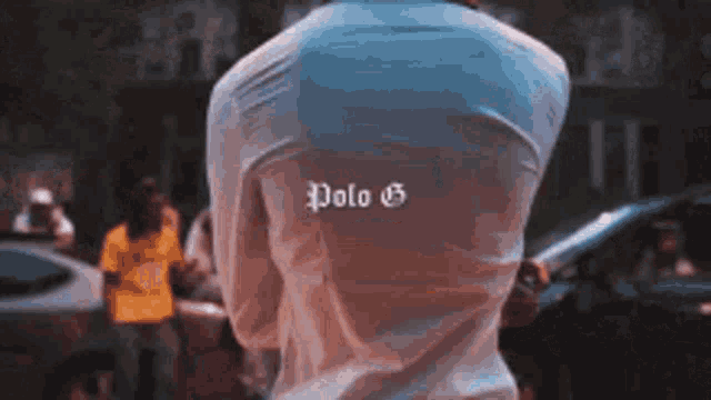 a man wearing a polo g shirt is standing in front of a crowd of people