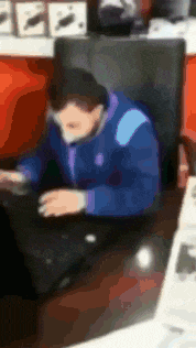 a man in a blue jacket sits at a desk using a laptop computer