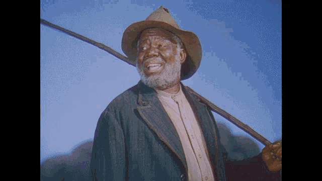 a man with a beard wearing a cowboy hat is holding a stick