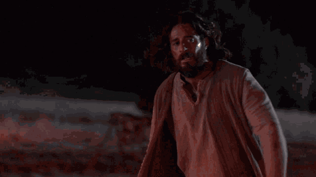 a man with a beard and long hair is standing in the dark