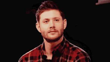 a man in a plaid shirt is smiling while holding a microphone in his hand .