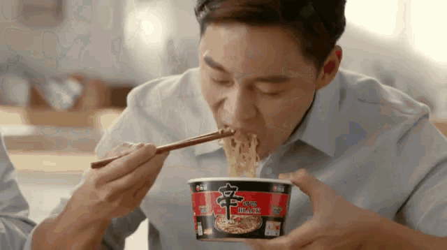 a man is eating a cup of noodles with chopsticks .