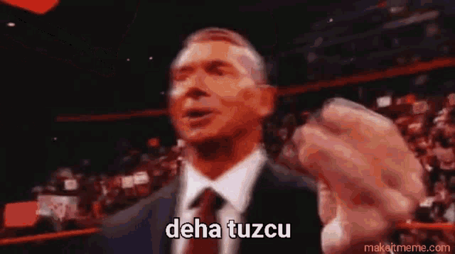 a man in a suit and tie says deha tuzcu in front of a crowd .