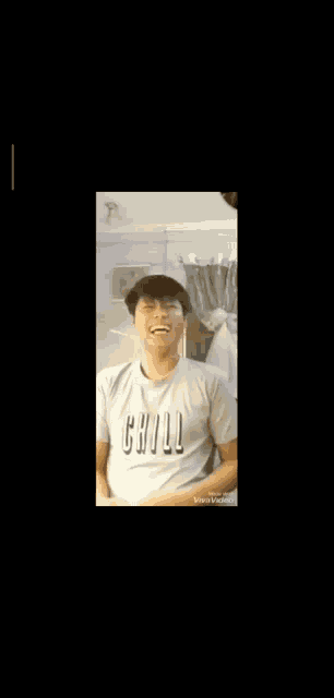 a man wearing a white t-shirt with the word chill on it is smiling and looking at the camera .