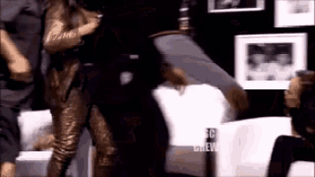a woman in a gold jumpsuit is dancing with a man in a chair .