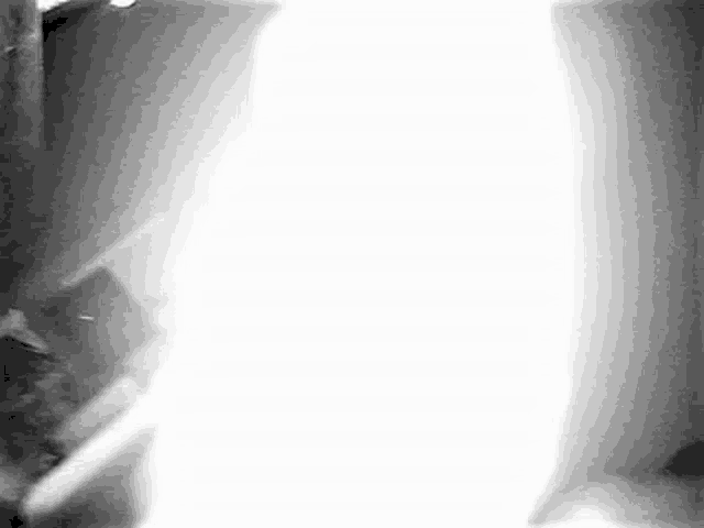 a black and white photo of a person standing in a dark room with a light coming through a window .