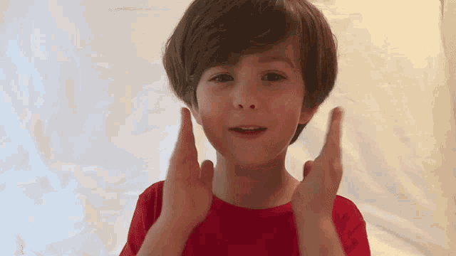 a young boy in a red t-shirt is clapping his hands