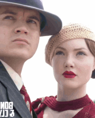 a man in a suit and tie stands next to a woman wearing a hat