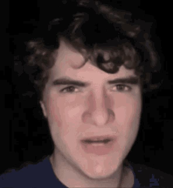 a young man with curly hair is making a funny face in a close up of his face .