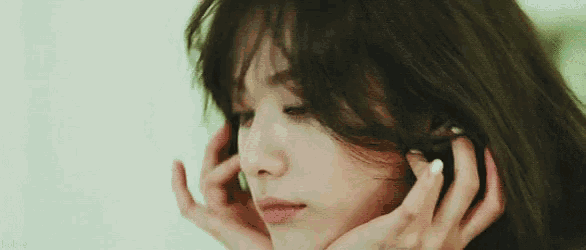 a close up of a woman 's face with her hands on her ear .