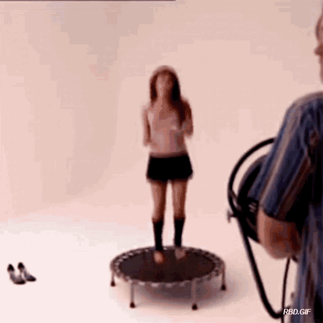 a woman is jumping on a trampoline while a cameraman takes a picture of her