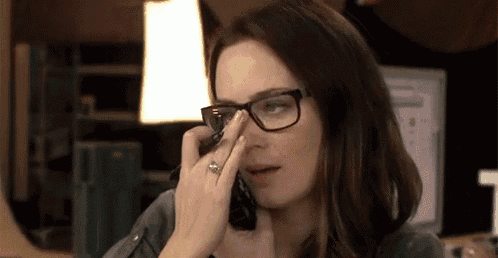 a woman wearing glasses is talking on a cell phone and cleaning her nose .