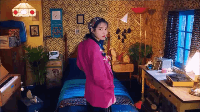 a woman in a pink jacket is standing in a bedroom next to a bed and a piano .