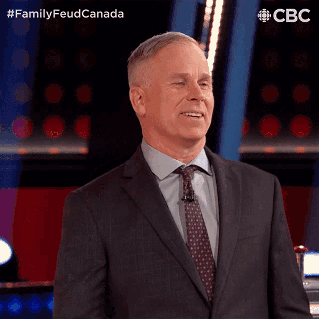 a man in a suit and tie stands in front of a screen that says cbc