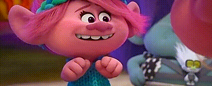 a troll with pink hair and a blue dress is standing next to another troll and smiling .