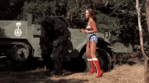 a woman in a wonder woman outfit stands in front of a military vehicle