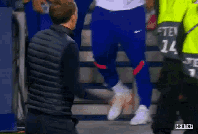a man in a black vest is standing next to a man in blue pants walking down stairs .