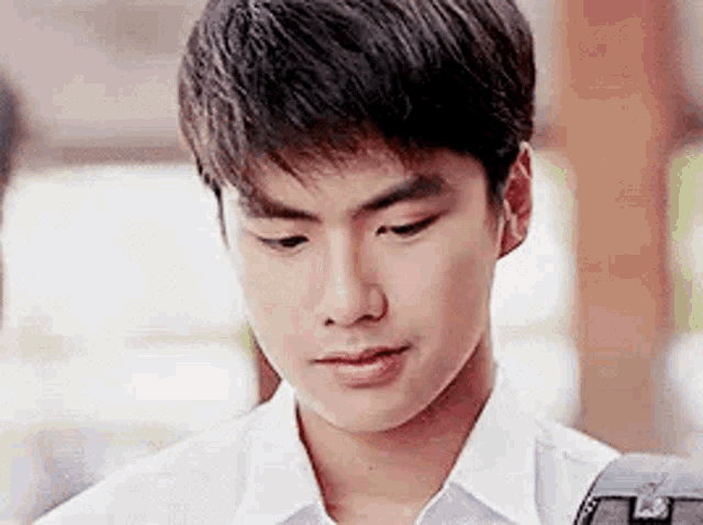 a close up of a young man in a white shirt looking down .