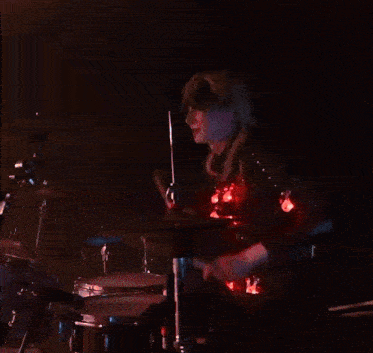 a woman playing drums in a dark room with a blue light behind her