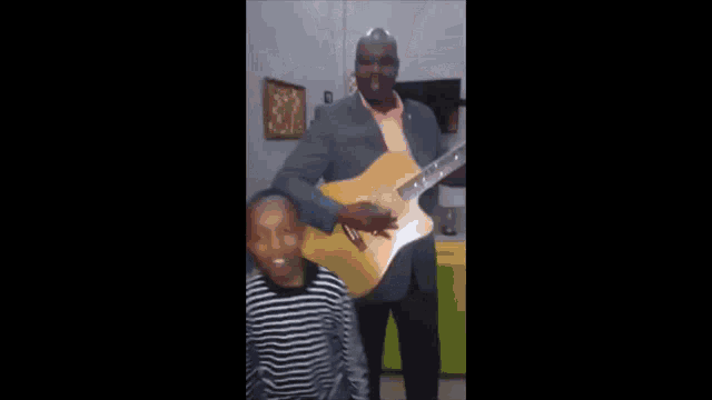 a young boy in a striped shirt is standing next to a guitar .