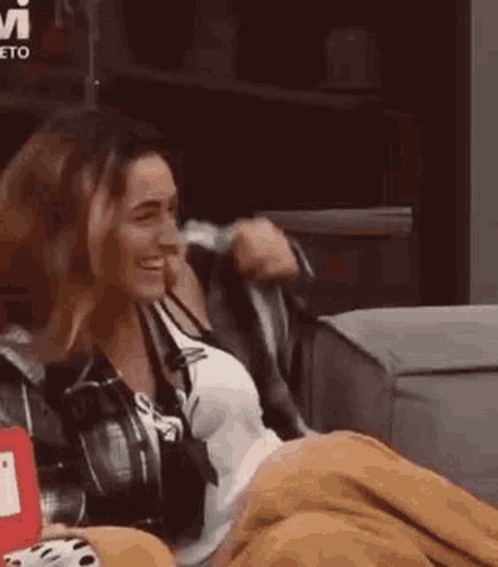 a couple of women sitting next to each other on a couch holding a blanket .