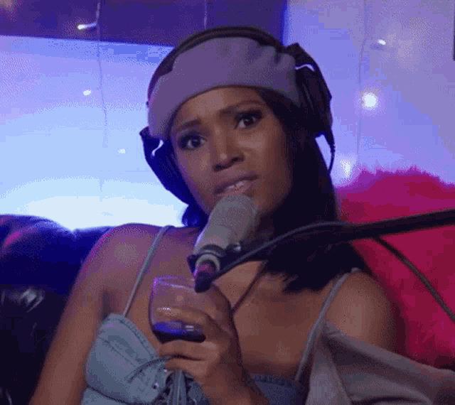 a woman wearing headphones holds a glass of wine in front of a microphone .