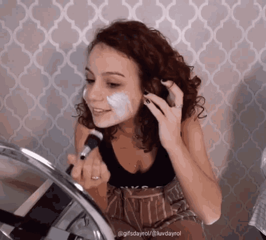a woman applying makeup in front of a mirror with the hashtag gifsdayrol on the bottom