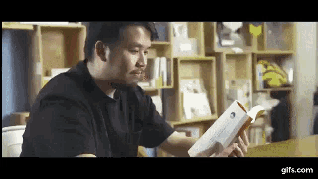 a man in a black shirt is reading a book in a library .