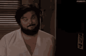 a man with a beard and mustache is making a funny face in a room .