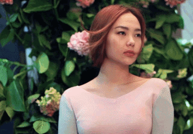 a woman in a pink dress stands in front of a bush of pink flowers