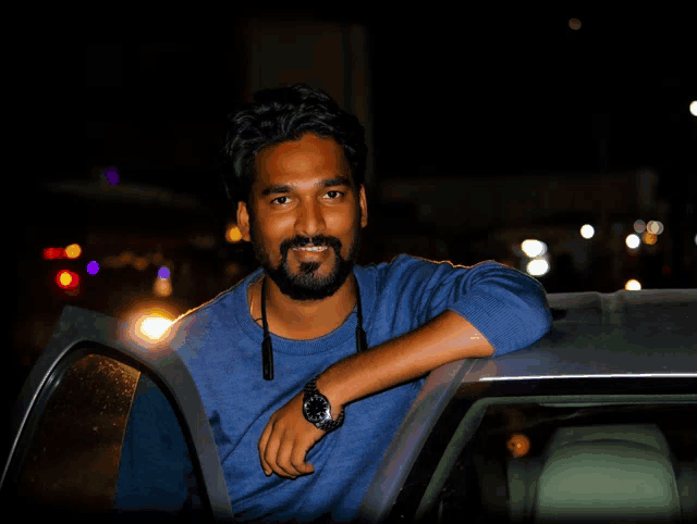 a man wearing a blue shirt and a watch leans on the door of a car