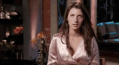 a woman in a pink dress is sitting at a table and making a funny face