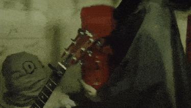 a person is playing a guitar in a dark room with a red fire extinguisher in the background .