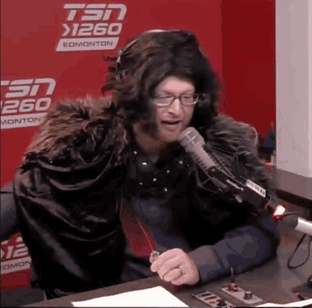 a man in a fur cape is sitting in front of a microphone ..