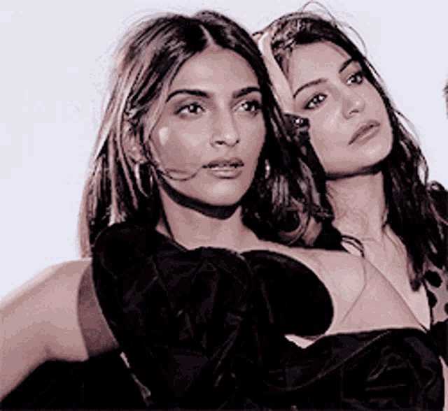 two women in black dresses are standing next to each other and looking at the camera