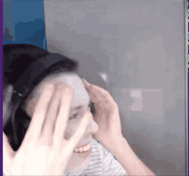 a person wearing headphones is covering their face with their hands and smiling .