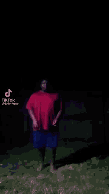 a man in a red shirt and blue shorts is dancing in a dark room .