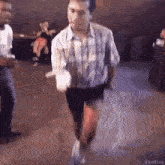 a man in a plaid shirt and shorts is dancing in a room .