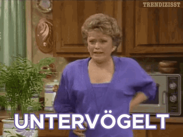 a woman in a purple shirt is standing in a kitchen with the word untervogelt on the screen